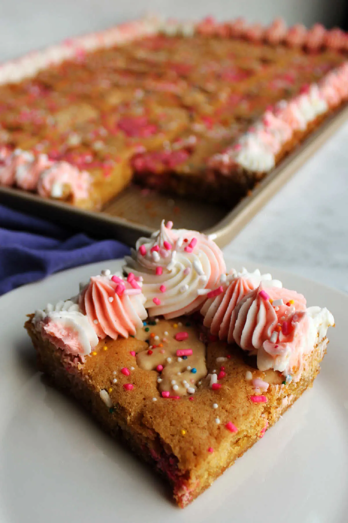 Square of frosted animal cracker blondies on a plate with frosting and sprinkles on top ready to eat. 