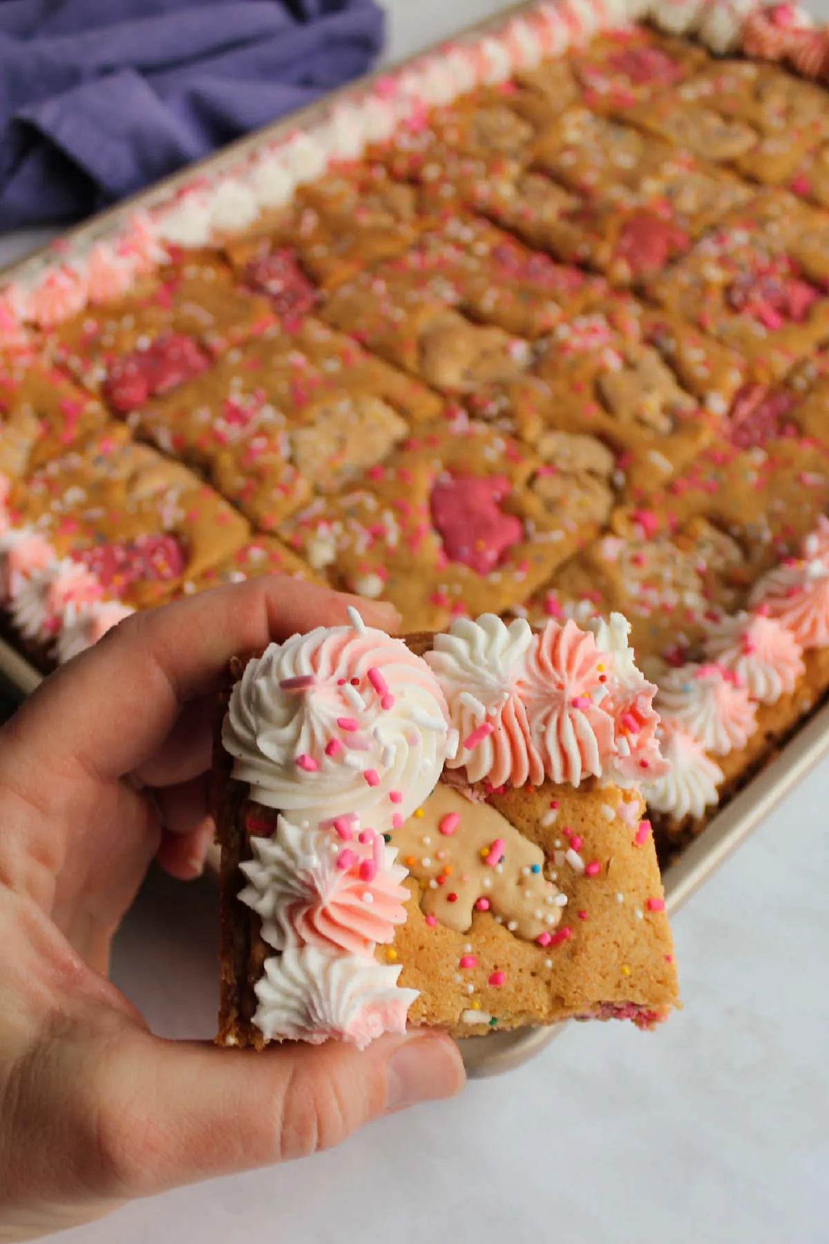 Hand holding circus animal blondie topped with swirls of pink and white buttercream and extra sprinkles.
