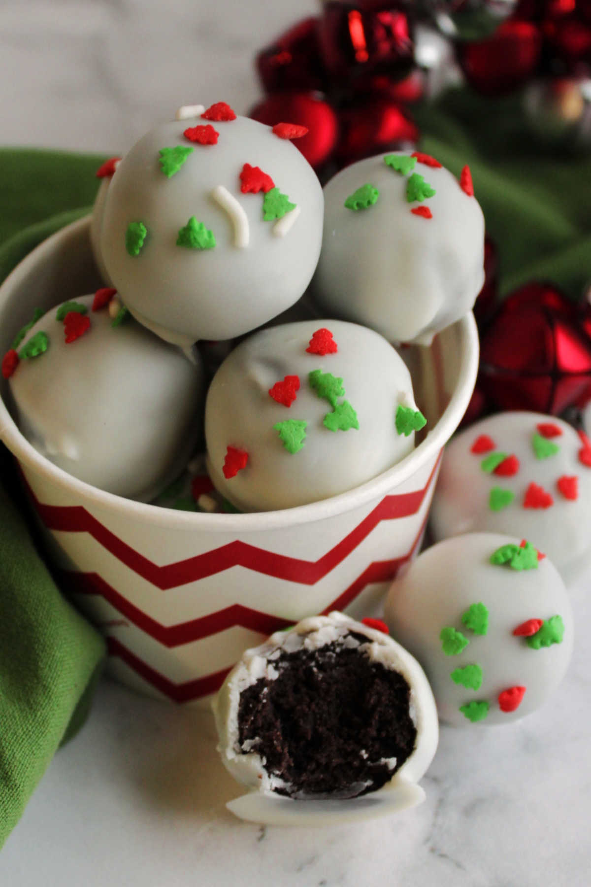 Red and white bowl filled with condensed milk oreo truffles with one missing a bite in the front showing the dark chocolate center. 