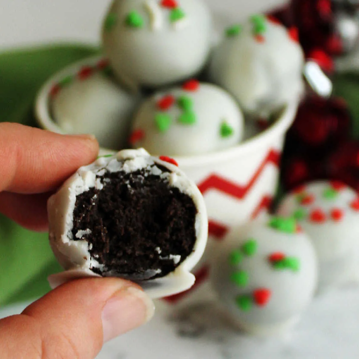 Hand holding white chocolate coated oreo truffle showing smooth center of oreo and condensed milk mixture.