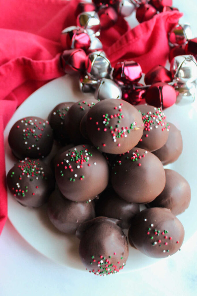 Plate piled high with sprinkle topped chocolate dipped peanut butter cookie balls. 