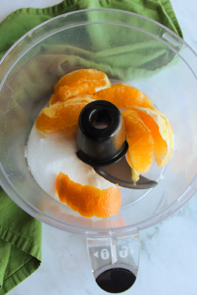 Orange sections and sugar in food processor bowl.