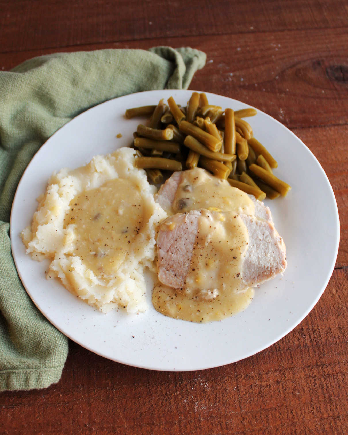 Slow cooker pork loin slices served with creamy gravy, mashed potatoes and gravy and green beans ready to eat.