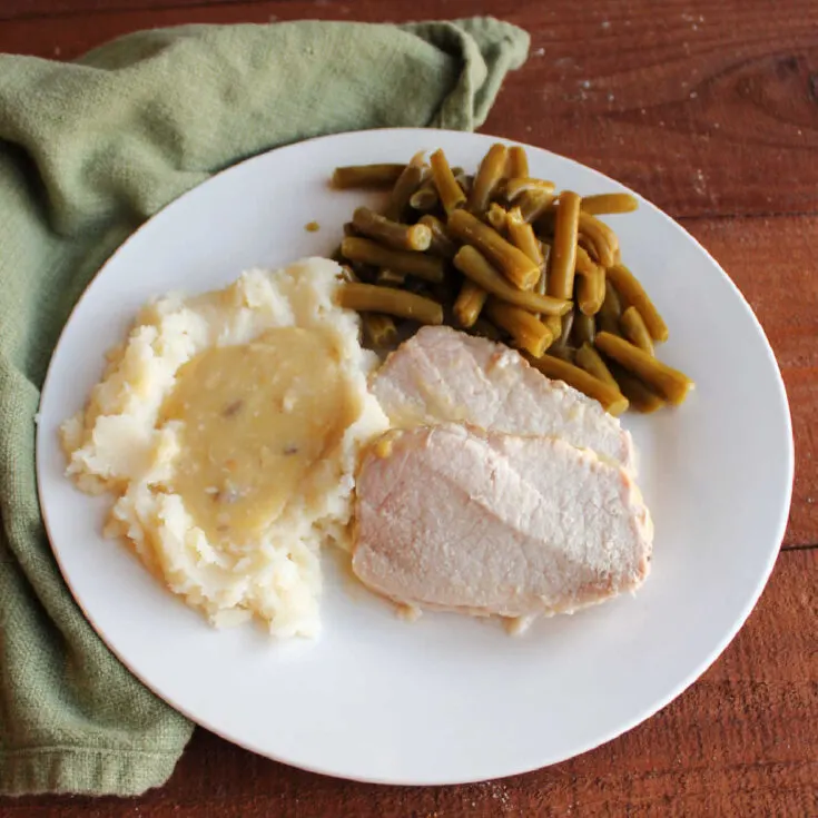 Dinner plate with slices of slow cooked pork loin, mashed potatoes and gravy and green beans.