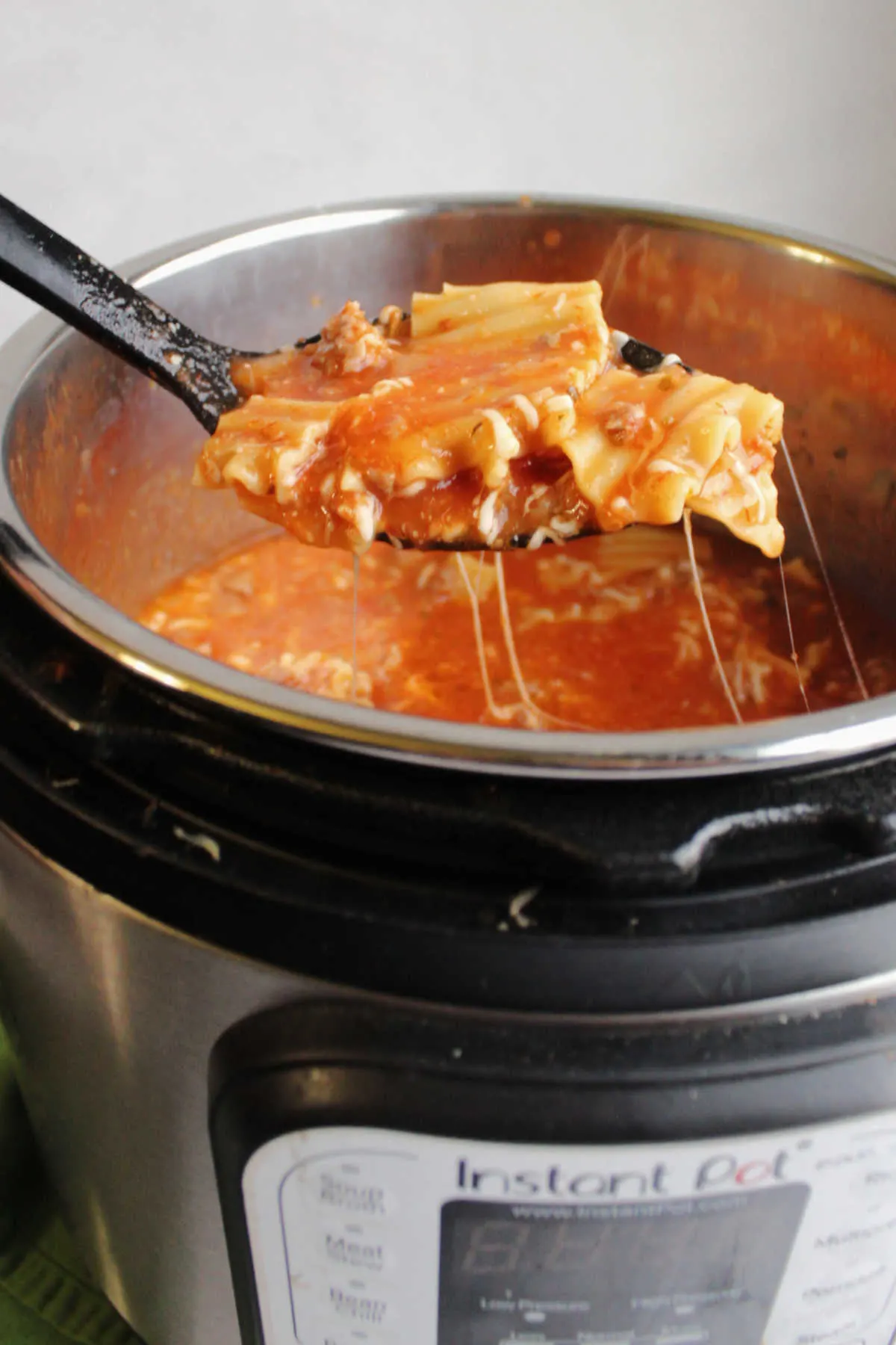 Scooping a helping of lasagna soup out of instant pot with cheese pulling out of the pot.