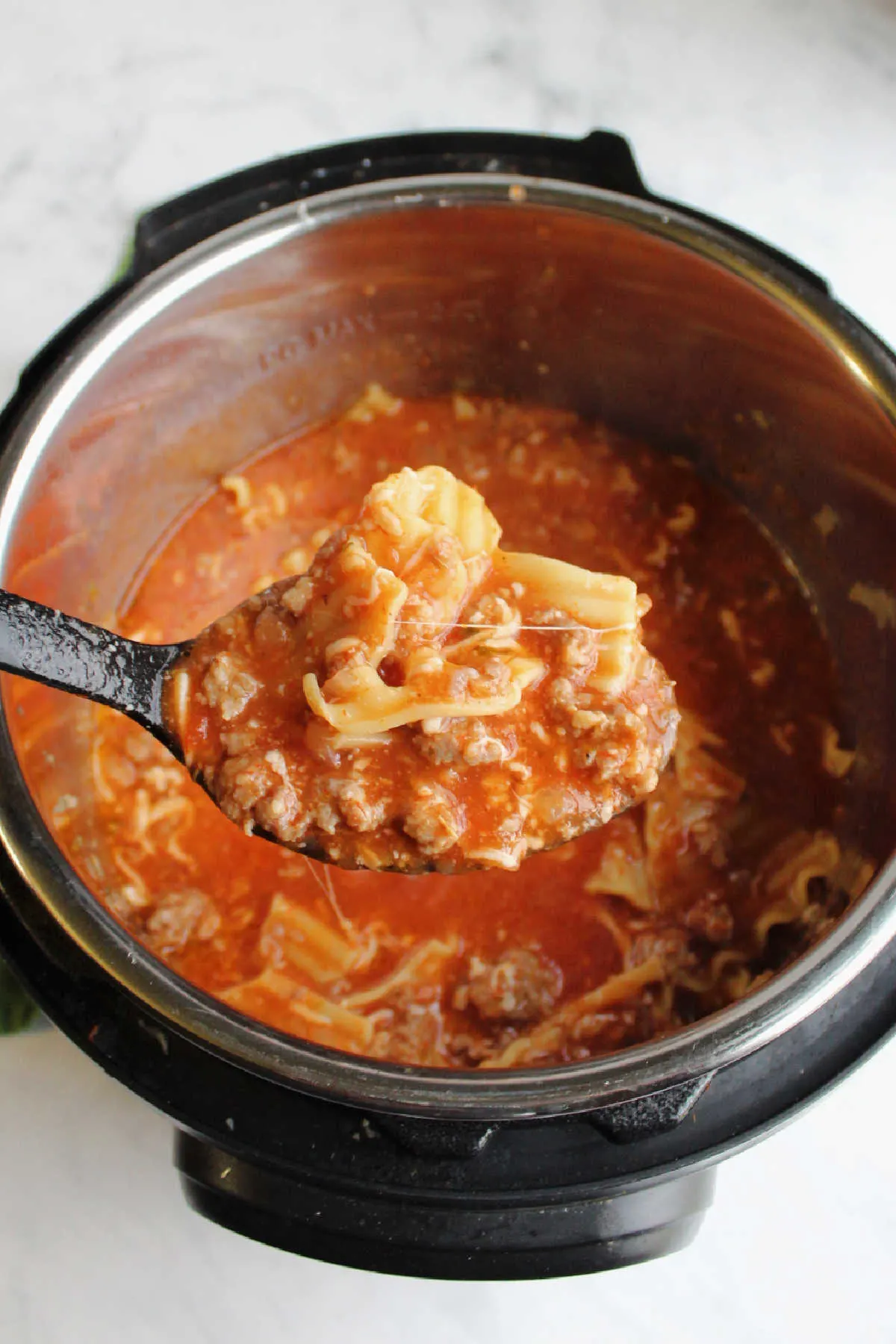 Large spoon scooping lasagna soup out of pressure cooker.