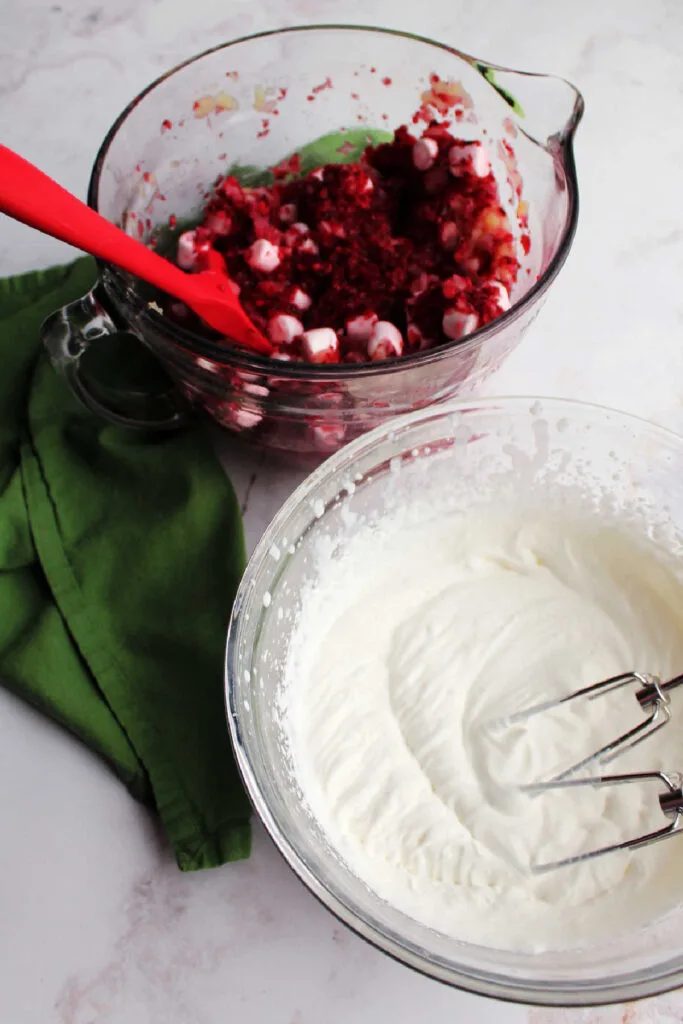 Bowl of whipped cream in front of bowl of cranberries, pineapple and marshmallow mixture