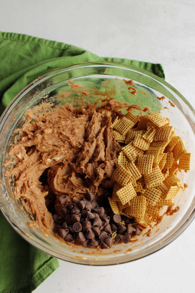 Adding Chex cereal and chocolate chips to muddy buddies dip.