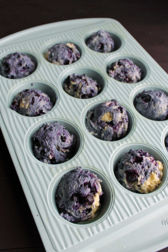 Blueberry muffin batter scooped into muffin pan.