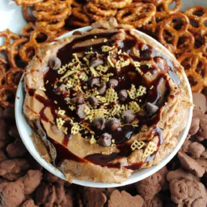 Close bowl of muddy buddies dip with chocolate and peanut butter served with pretzels and chocolate teddy grahams.