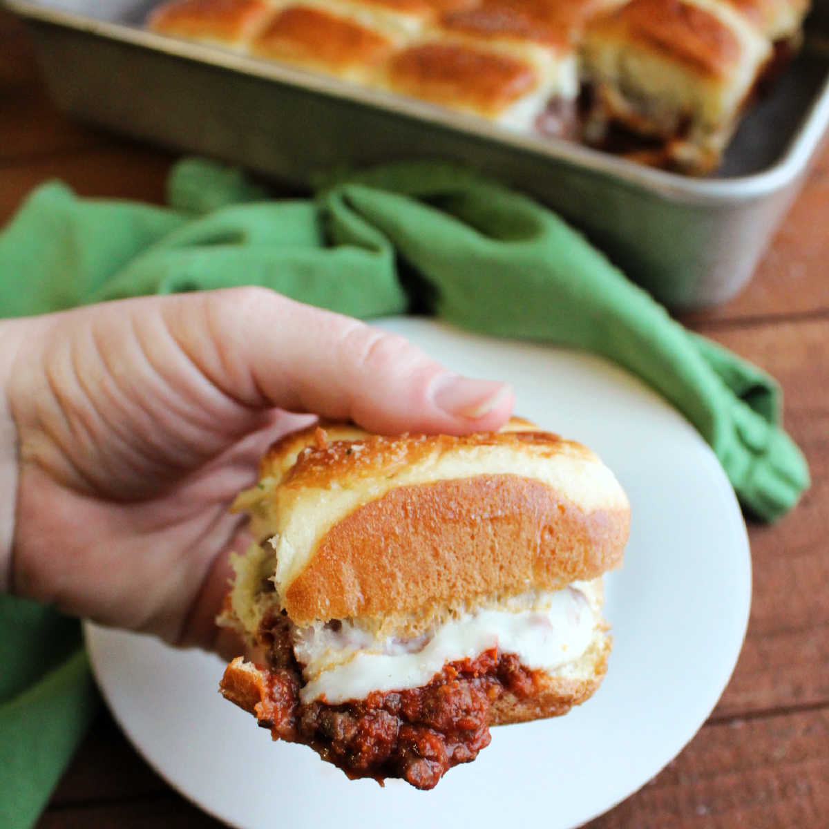 Hand holding pizza burger slider with melty cheese and garlic butter coated bun.