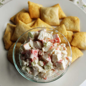 Bowl of imitation crab salad on plate with pita chips ready to eat.