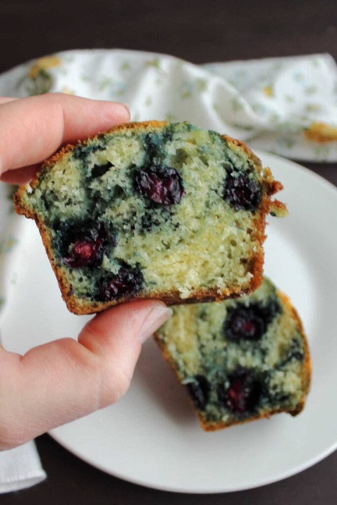 Hand holding half of a blueberry muffin.