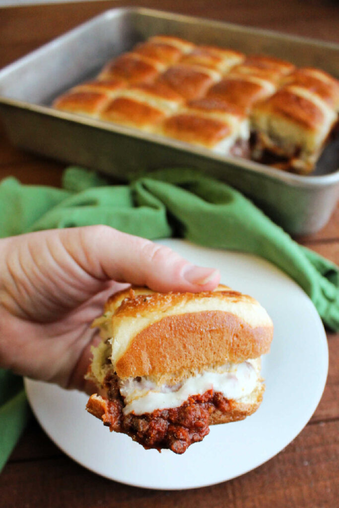 Hand holding slider filled with saucy meat mixture, melted cheese and garlic butter on top.