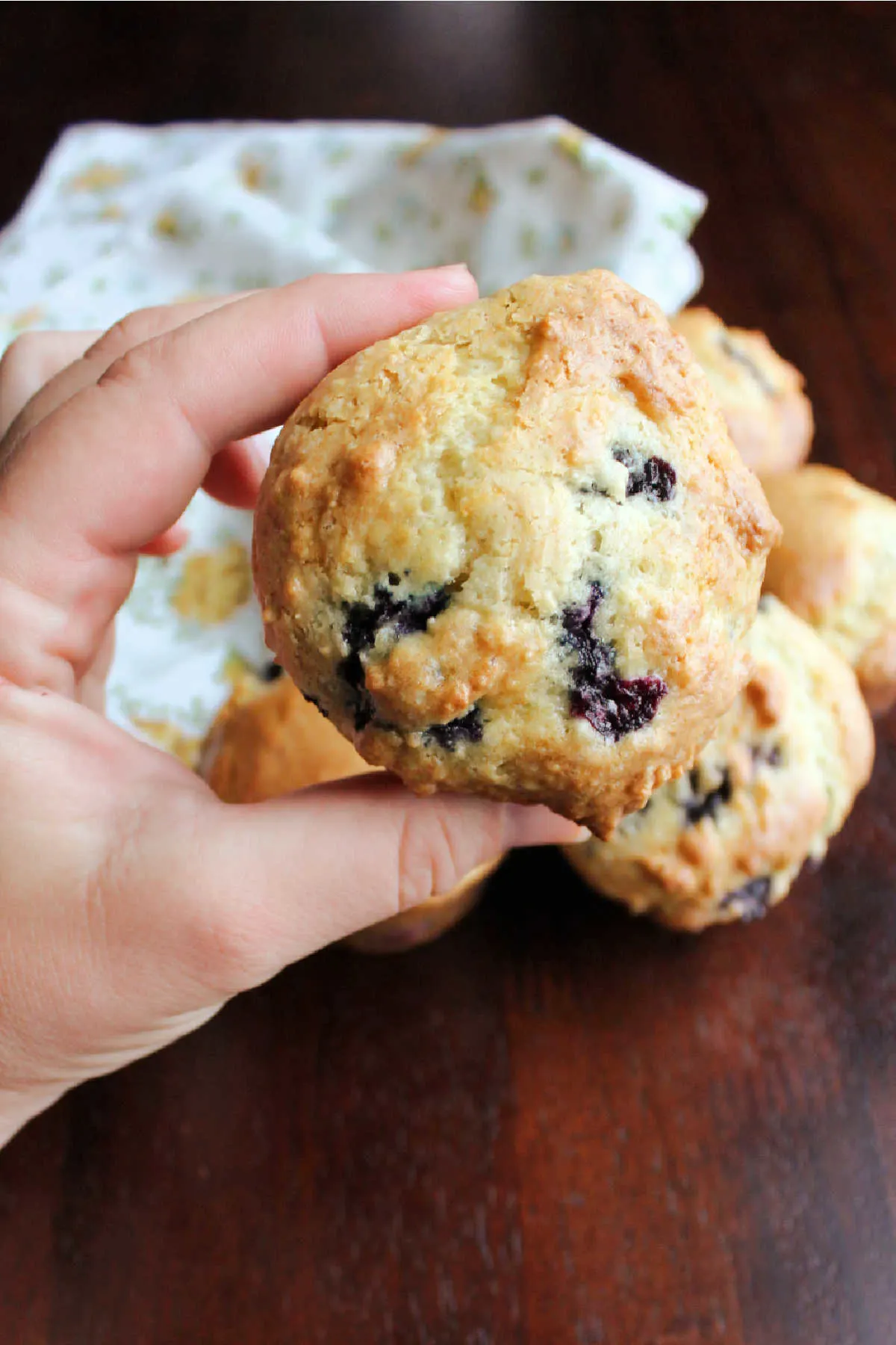Hand holding whole blueberry muffin with soft sour cream batter and lots of fresh berries.