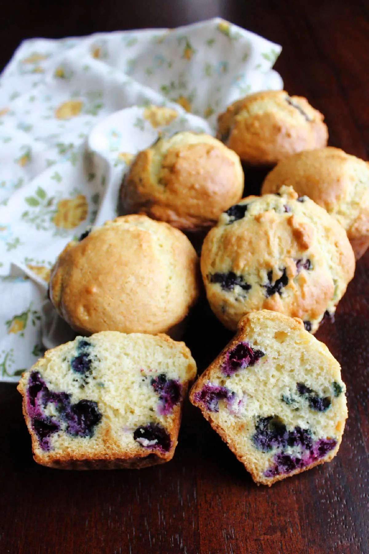 pile of fresh baked muffins with one cut in half showing berries and soft interior.