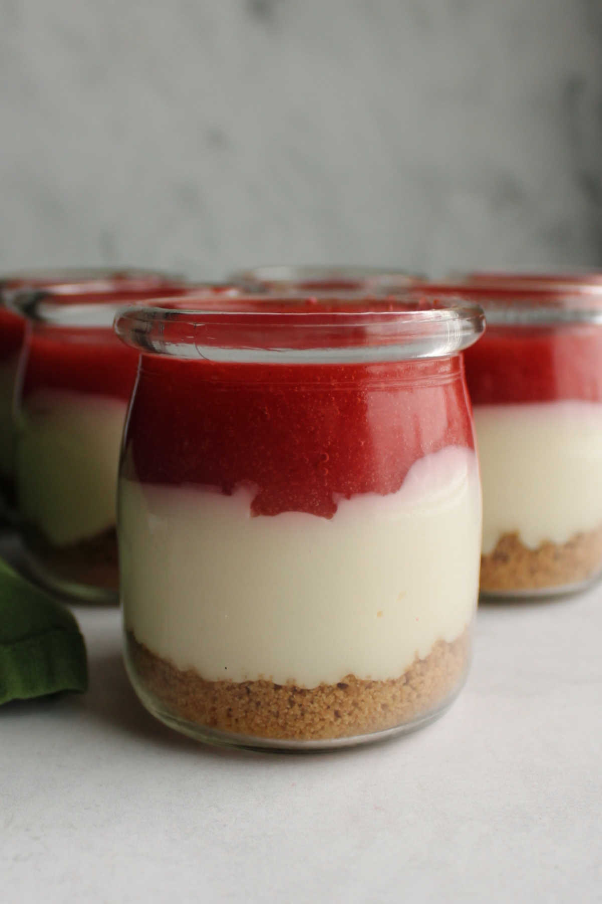 Jar filled with graham cracker crust, no bake cheesecake mixture and strawberry sauce.