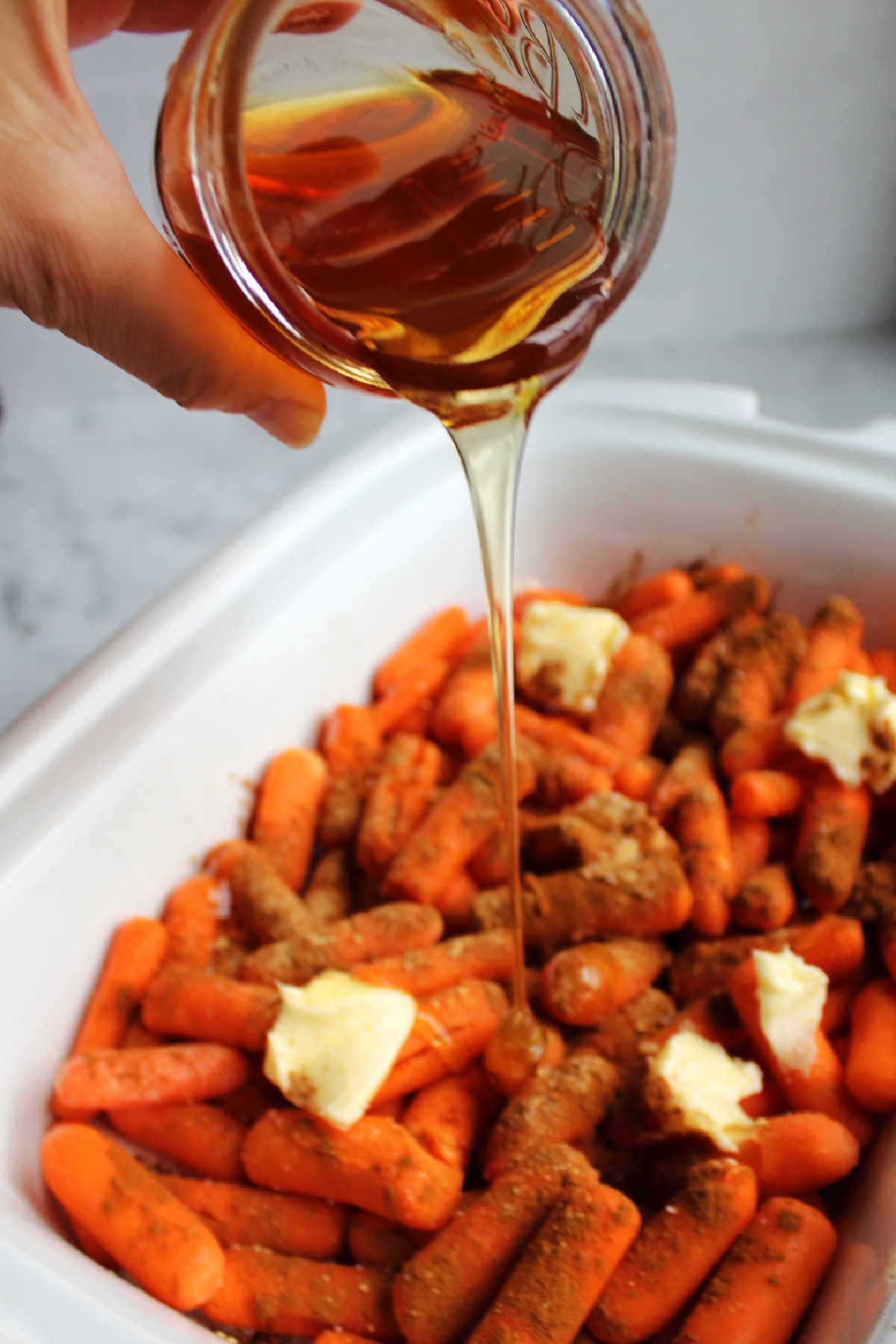 Pouring honey over carrots in slow cooker.