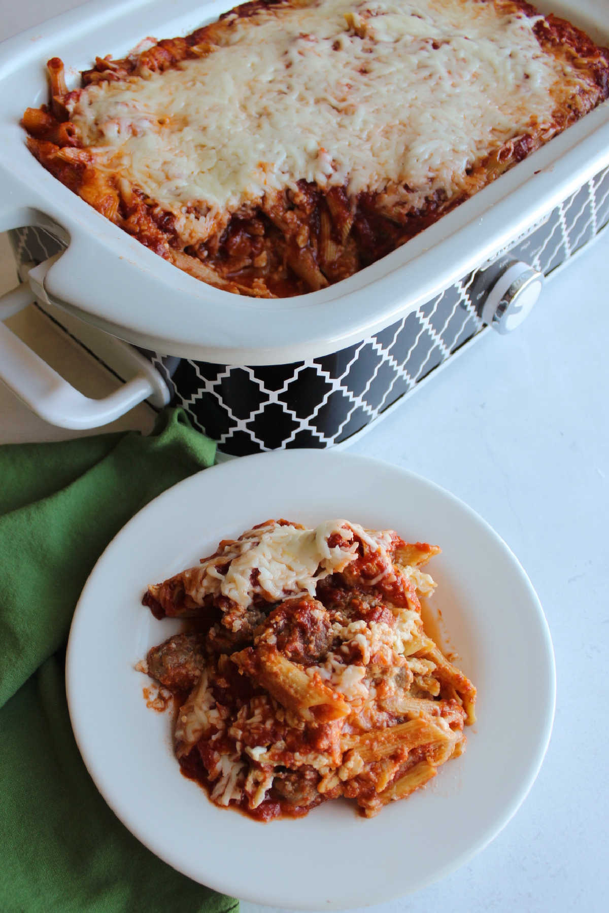 Baked penne with Italian sausage and cheese next to slow cooker filled with more baked pasta.