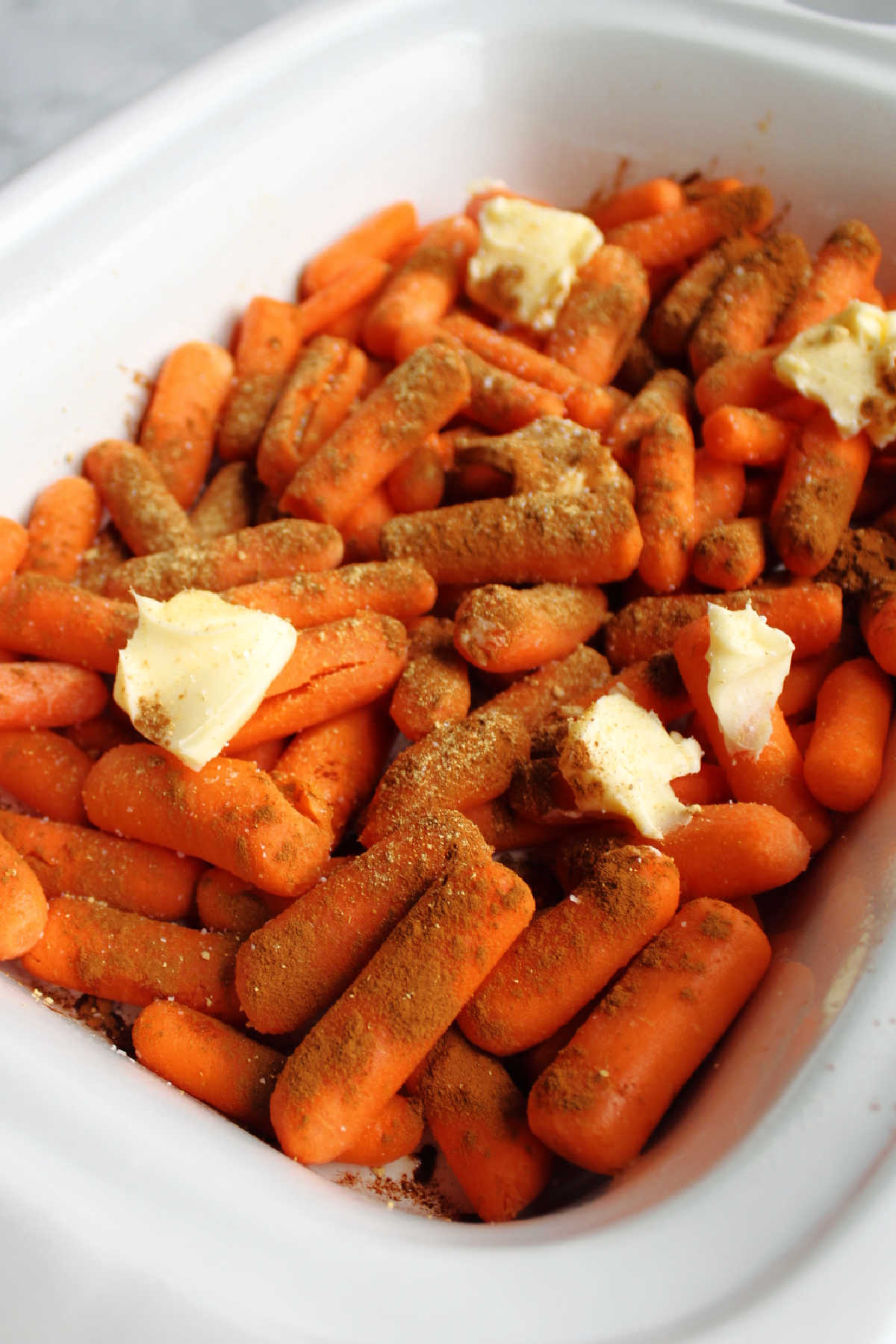Carrots topped with cinnamon and butter in slow cooker.