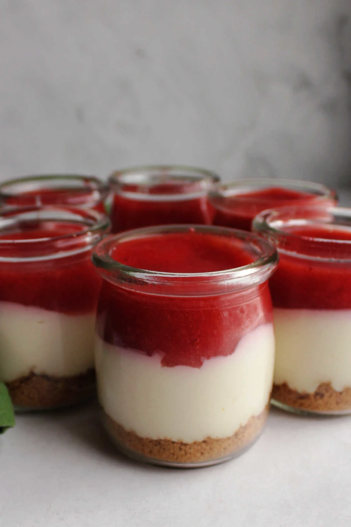 Collection of no bake cheesecake jars topped with strawberry sauce.