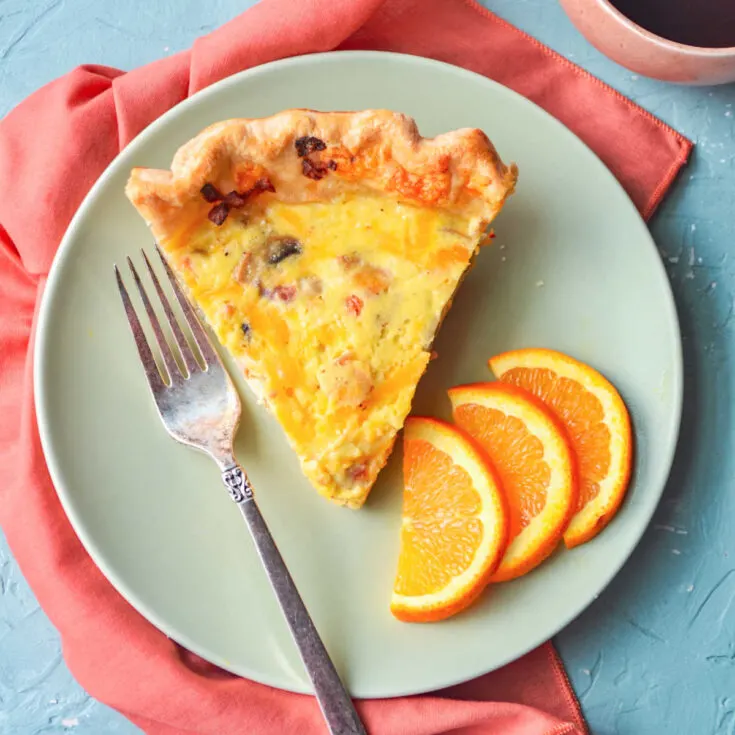 Plate with slice of bacon quiche and orange slices.