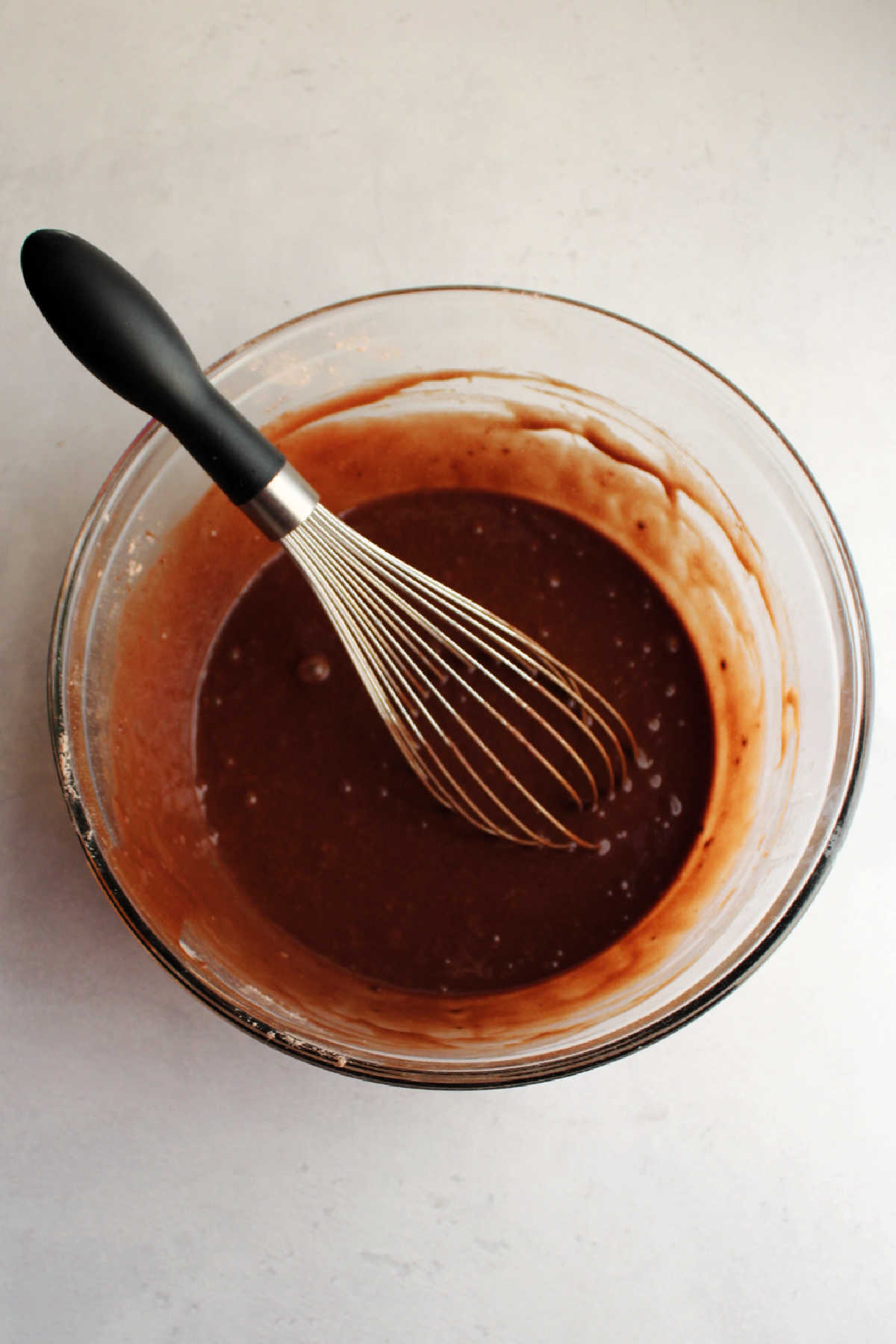 Mixing bowl with chocolate cake batter and whisk.