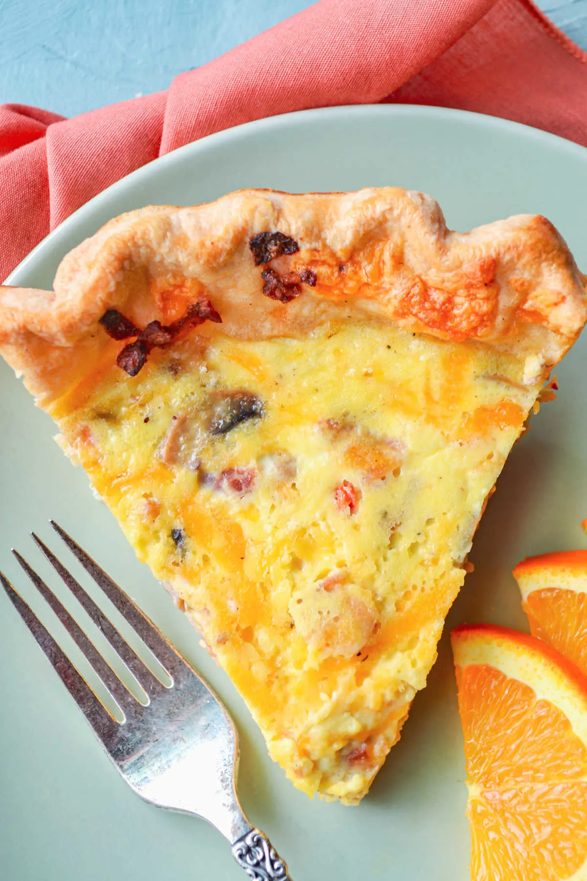 Looking down on a slice of quiche with bits of bacon, red pepper, onion and mushrooms baked inside. 