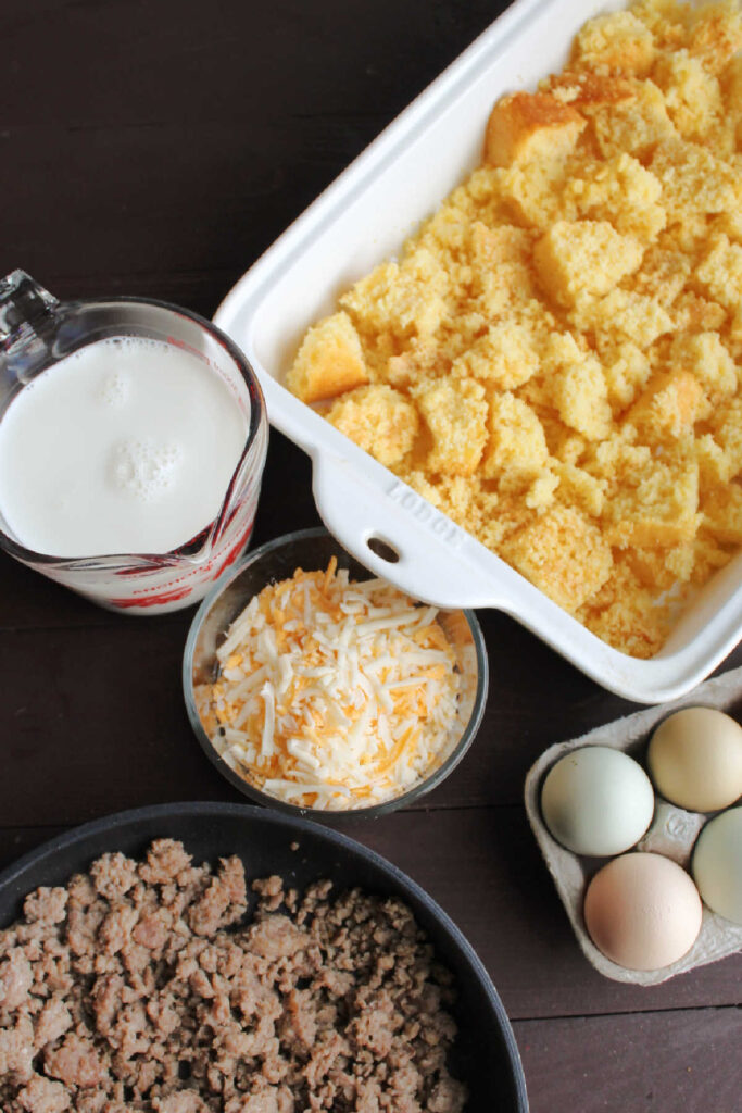 Ingredients ready to be made into cornbread egg casserole (eggs, cheese, milk, sausage and cubes of cornbread).