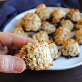 Hand holding a pistachio coconut macaroon with flecks of golden brown on the exterior.