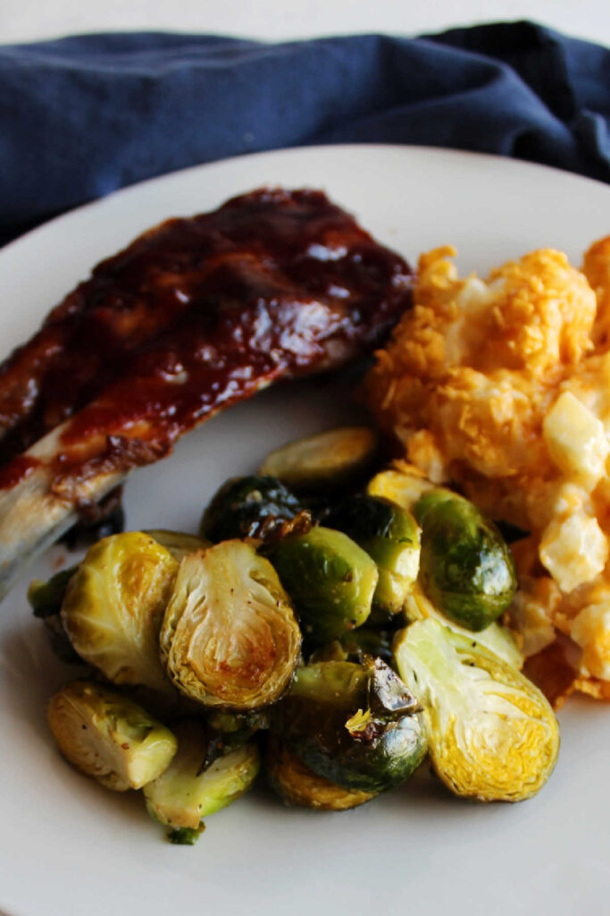 Close up of roasted brussels sprouts on plate with cheesy potatoes and BBQ ribs.