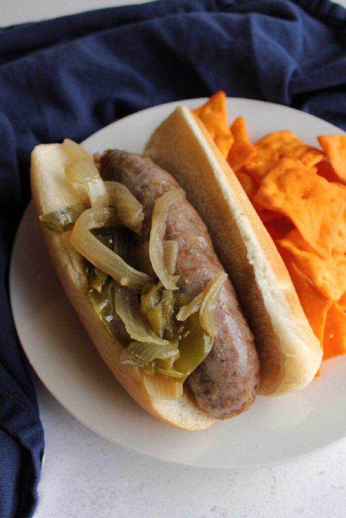 Brat served with onions and peppers served with cheesy chips on dinner plate. 