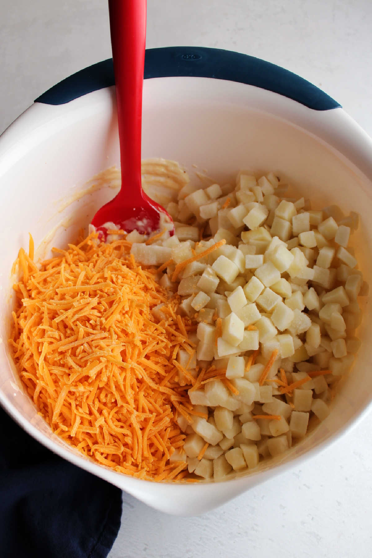 Shredded cheddar and cubes of potato in bowl with ranch mixture.