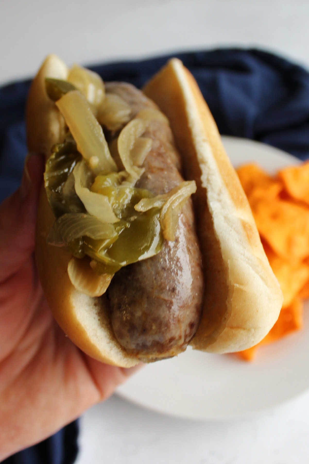 Side view of a hand holding brat with peppers and onions ready to eat. 