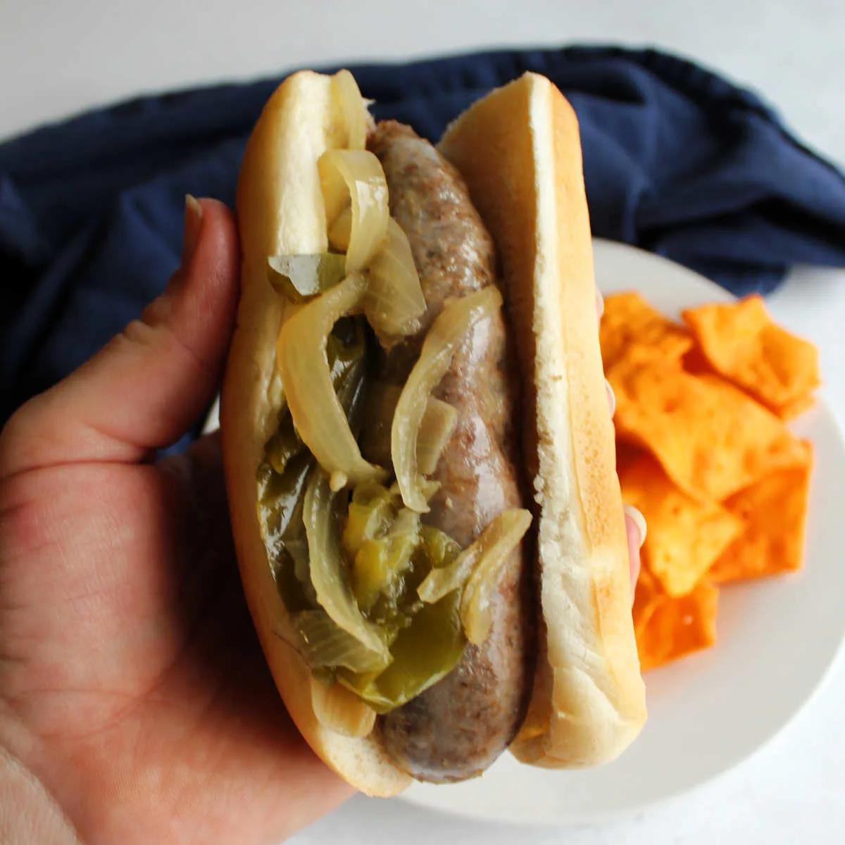 Hand holding bun filled with a brat and cooked onions and green peppers.