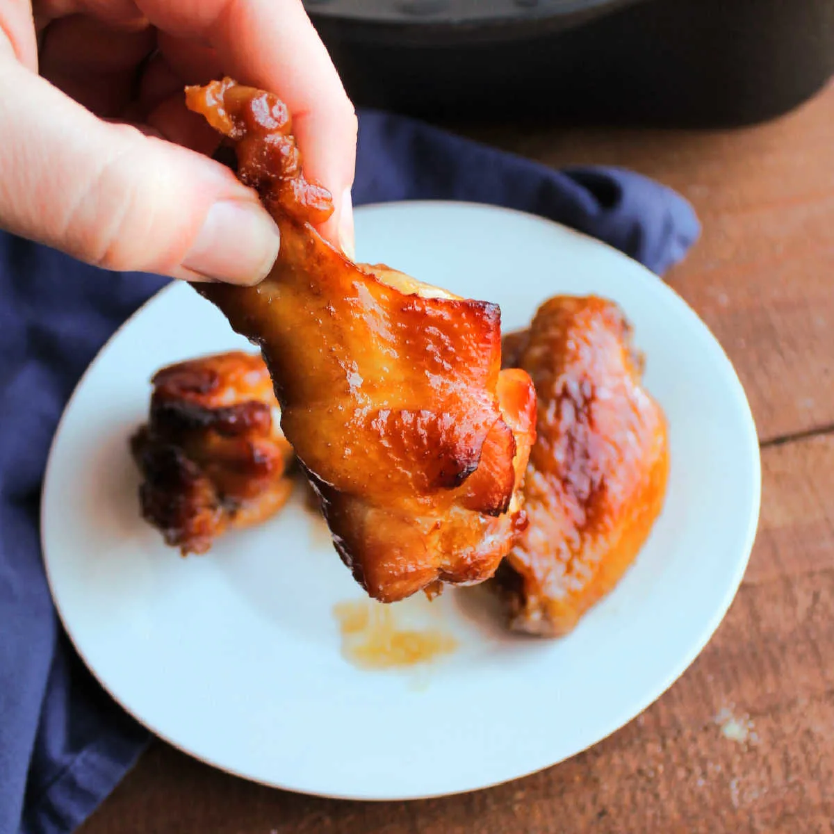 Hand holding golden brown chicken wing with sticky sauce on it.