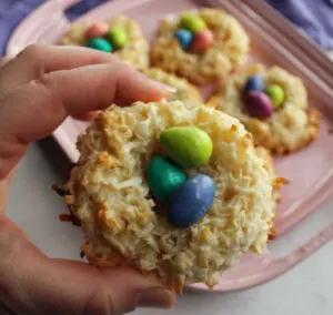 Hand holding coconut macaroon nest filled with candy eggs.