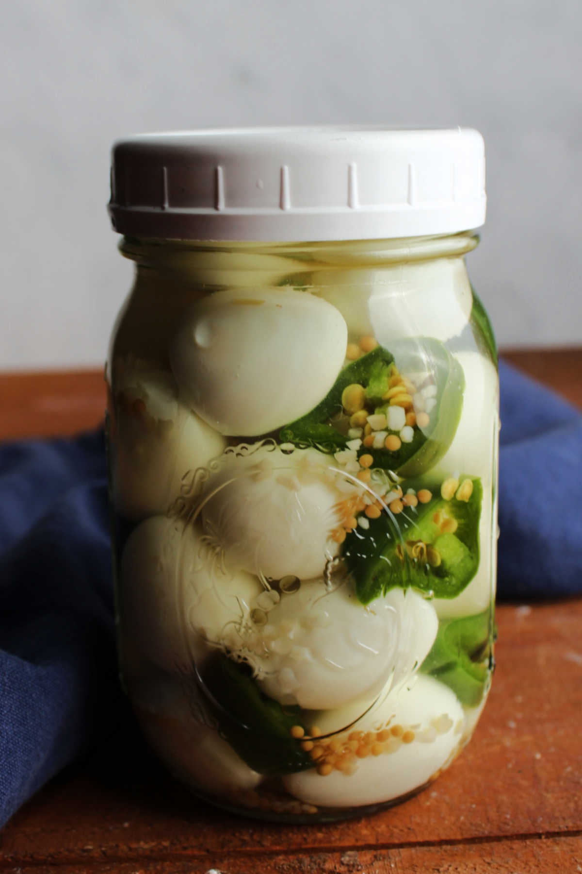 Glass pint jar filled with quail eggs, sliced jalapeno pepper and vinegar pickling liquid.