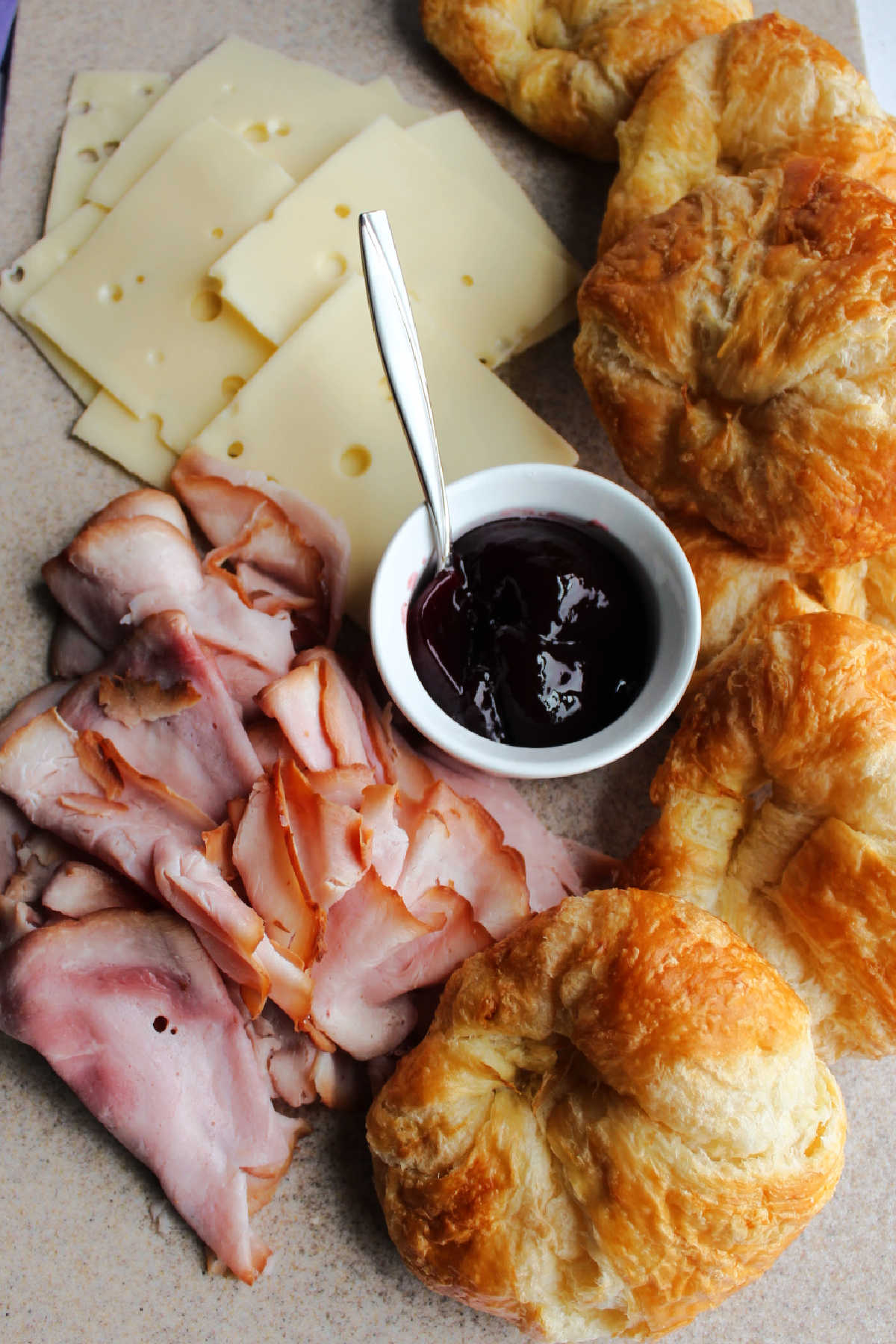 Tray of croissants, ham, swiss cheese and raspberry preserves.