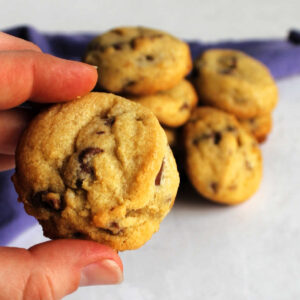 Hand holding a thick golden brown chocolate chip cookie.