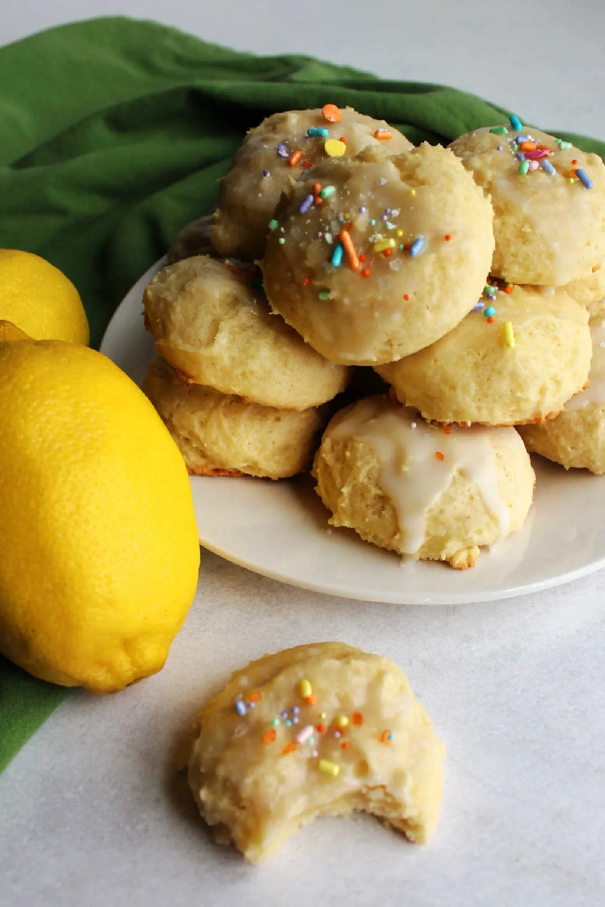 Pile of pillowy lemon cookies topped with white icing and sprinkles.