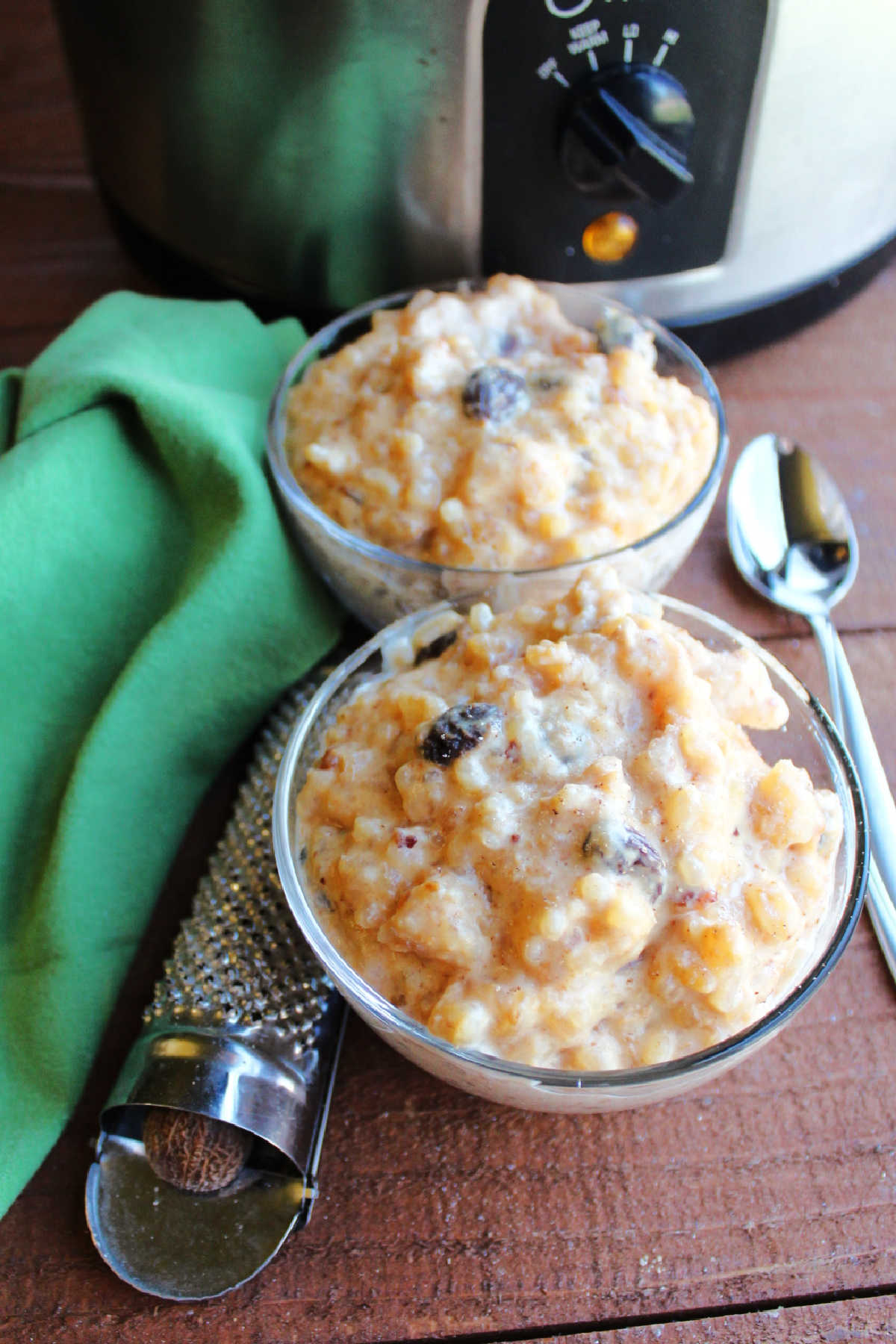 Bowls of condensed milk rice pudding with spoons and nutmeg grated by crockpot.