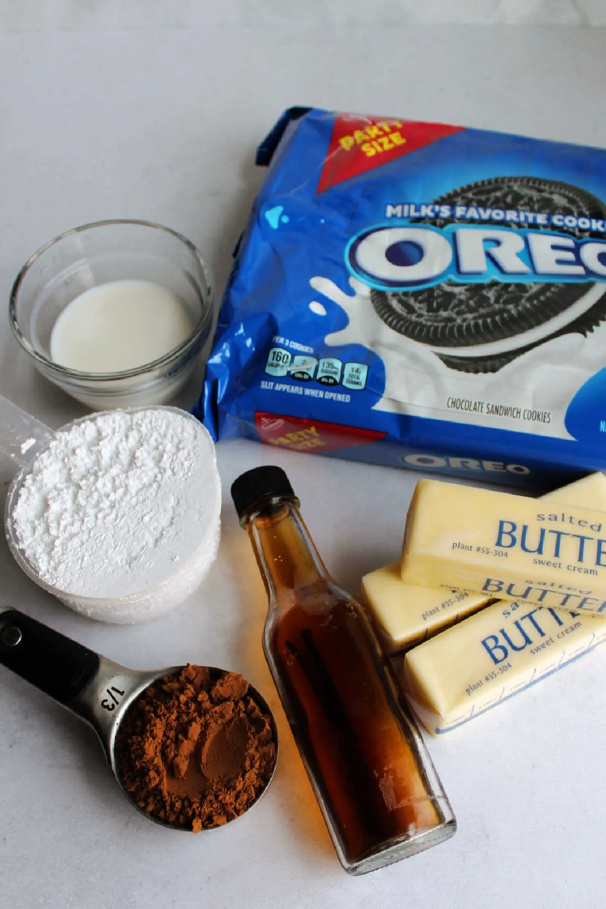 Ingredients including butter, powdered sugar, cocoa powder, vanilla, milk and Oreo cookies ready to be made into frosting.