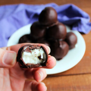 hand holding a homemade mounds candy showing the creamy coconut center and chocolate shell.