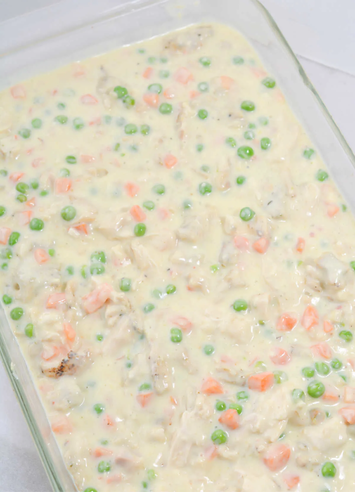 Creamy mixture with chicken and vegetables in pan.