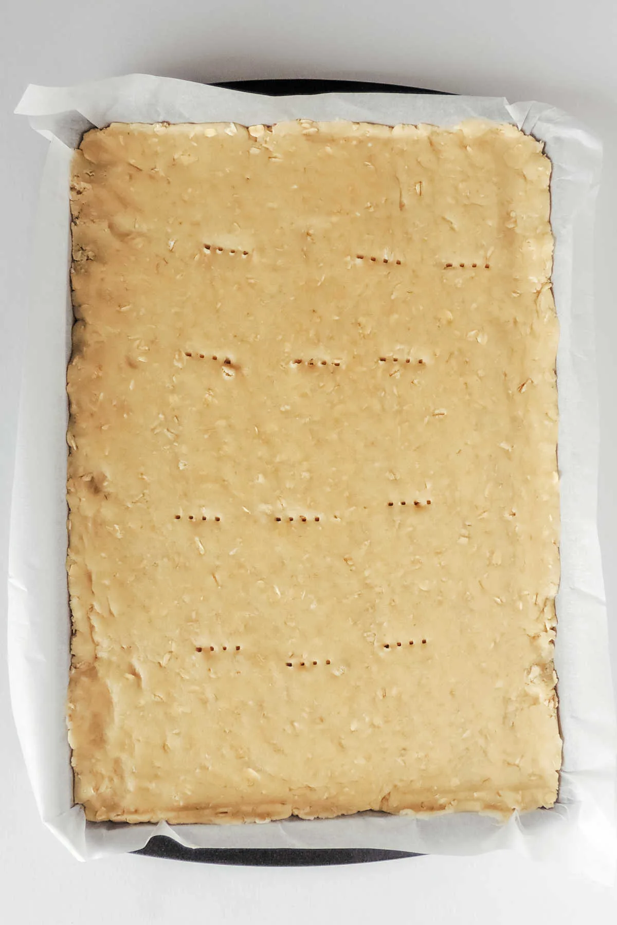 Cookie dough pressed into parchment lined cookie sheet with fork holes pricked into the top.
