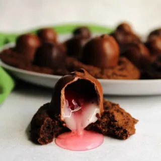 Chocolate cookie topped with chocolate covered cherry with bite out showing gooey insides.