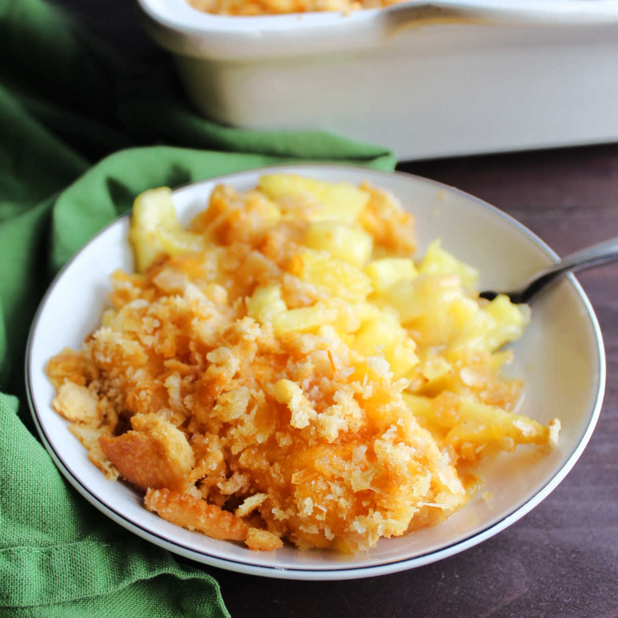 Small dish filled with pineapple casserole topped with buttery cracker crumbs and cheese.