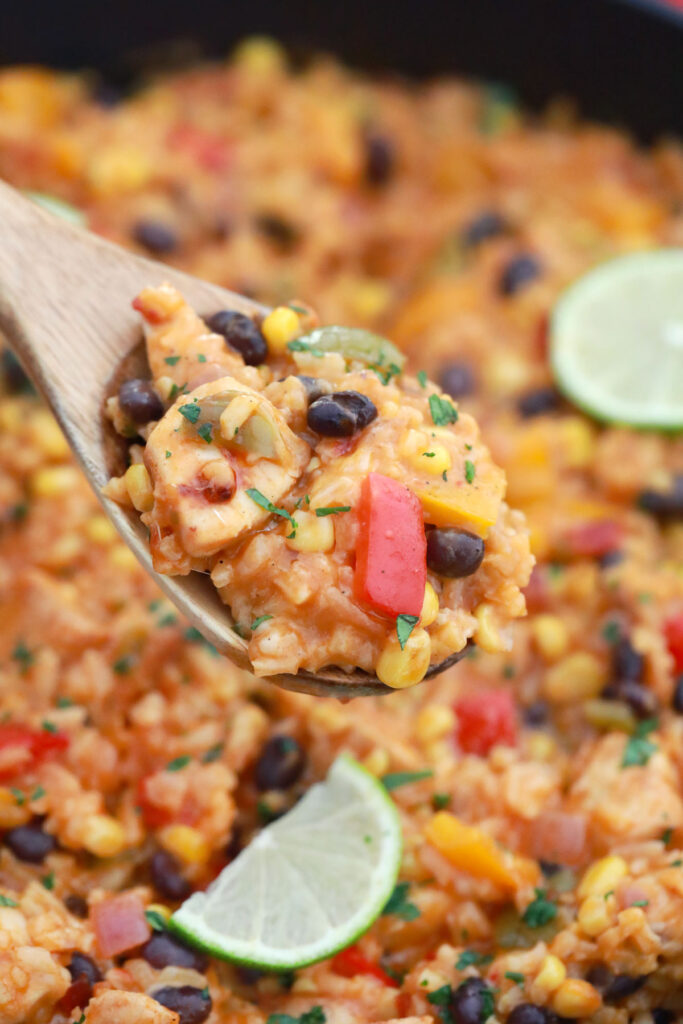 Serving spoon filled with tex-mex chicken and rice with beans and peppers, ready to be served.