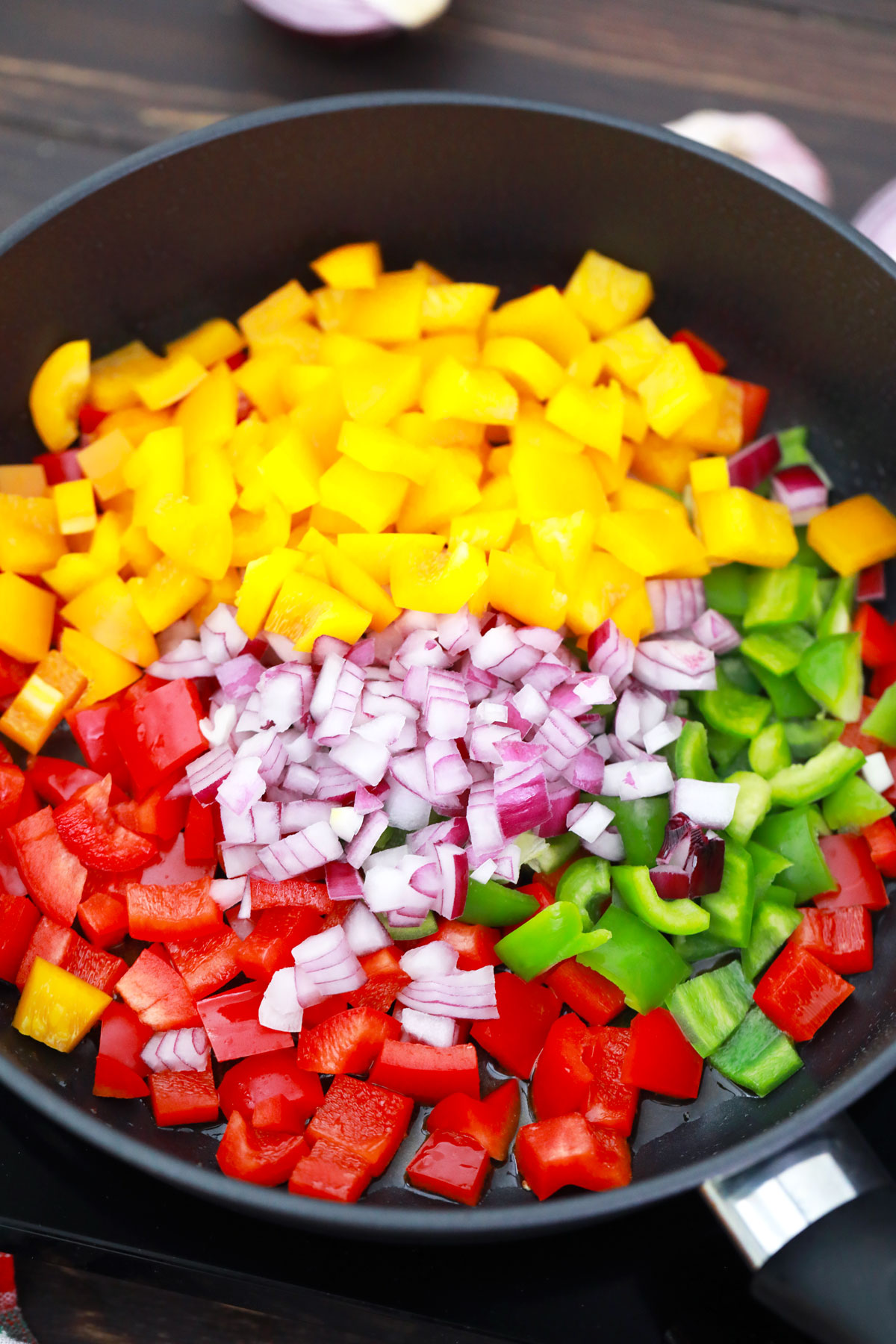 Colorful diced peppers and onions in skillet, starting to cook.